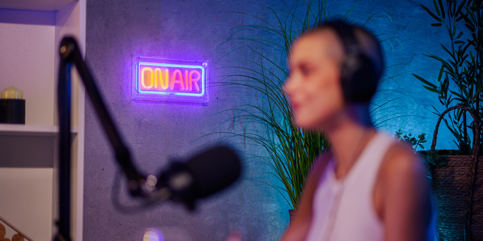 Woman recording a podcast with a microphone and a neon 'on air' sign in the background